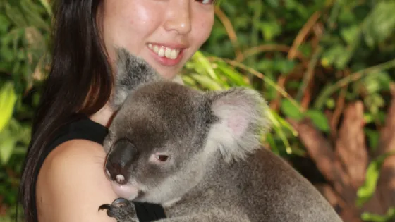 A woman smiling while holding a koala in a natural setting.