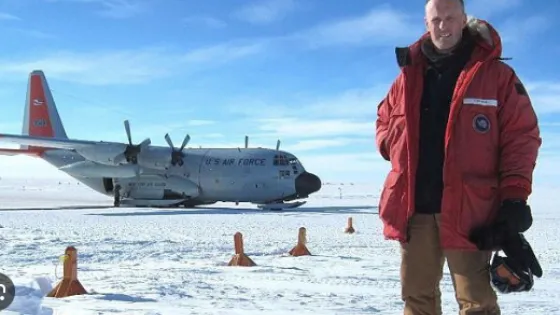 A person in a red jacket standing in the snow with a U.S. Air Force plane in the background.