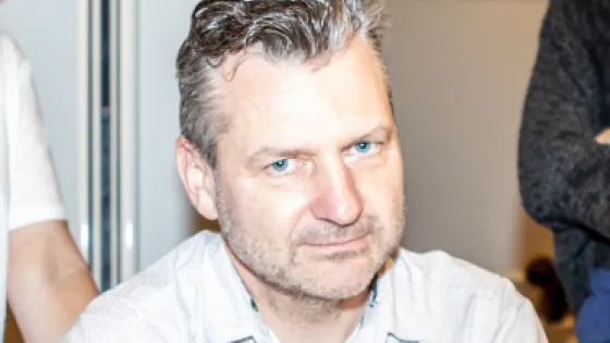 A man with graying hair and a focused expression sitting indoors.