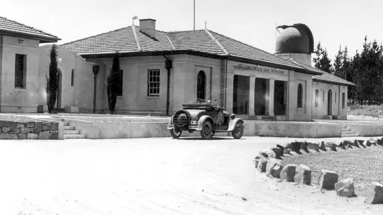 Black and white photo of old car in front of original builiding.