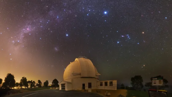 An observatory under a starry night sky, with the Milky Way galaxy visible above.